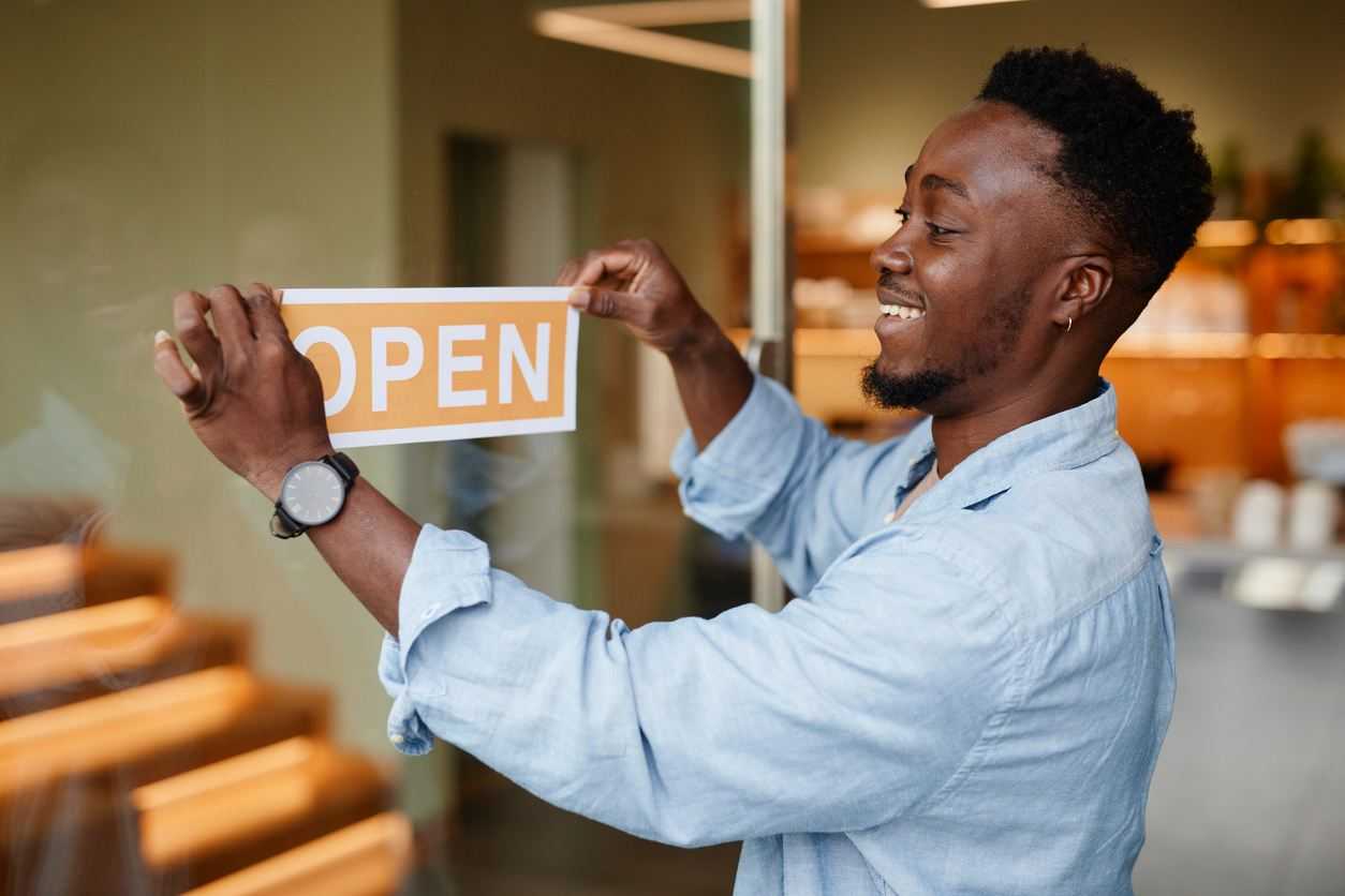 A smiling man puts up an open sign on a window.