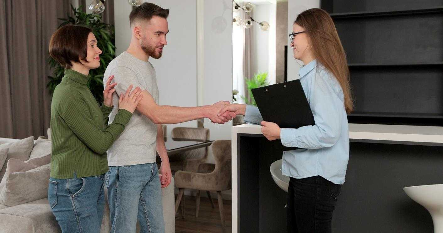 A landlord shakes the hands of new tenants while holding a signed lease