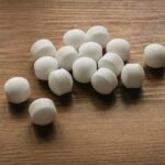 A group of white mothballs scattered on a wooden surface, commonly used for pest control.