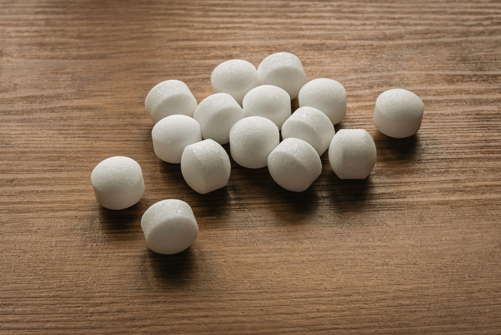 A group of white mothballs scattered on a wooden surface, commonly used for pest control.