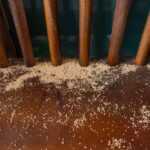 A close-up of a wooden surface with scattered termite feces beneath vertical wooden bars, showing clear signs of termites and indicating a possible termite infestation.